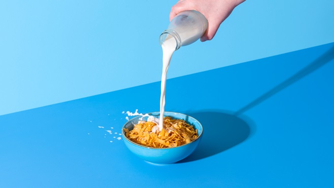 milk being poured into a bowl of corn flakes on a blue surface